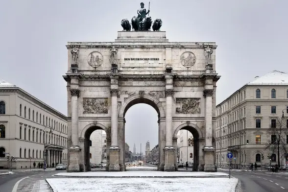 The image depicts the Siegestor (Victory Gate) in Munich, Germany. It is a large neoclassical arch that honors the Bavarian army. The monument is often noted for its grand size and intricate sculptures, and it's located in a snowy setting, indicating winter weather. The surrounding area includes roads, buildings, and possibly hints of urban life.

Image Credits: Wikimedia / Hendrik Schöttle / CC BY-SA 3.0