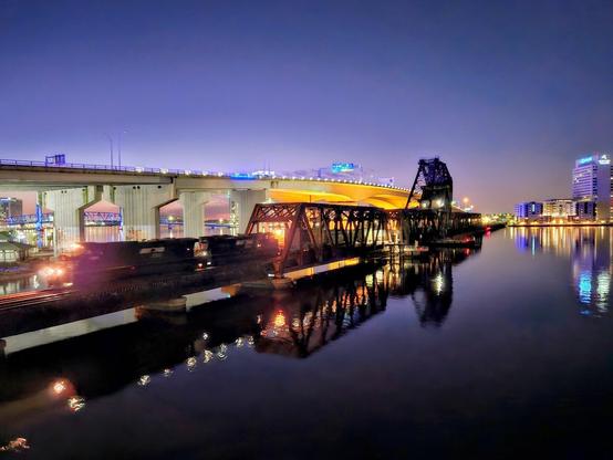 Late night train passes over the Saint Johns River, near downtown Jacksonville, Florida.  The city skyline, adjacent traffic bridge, and the trestle itself glow with lighting against the dark blue night skies, and reflect onto the still waters below.