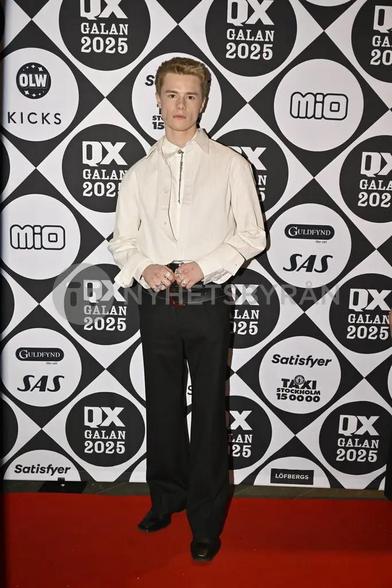 Le même, mâchoire serrée, posant sur le tapis rouge avant le gala. On voit ses nombreuses bagues, et une étrange double ceinture.
