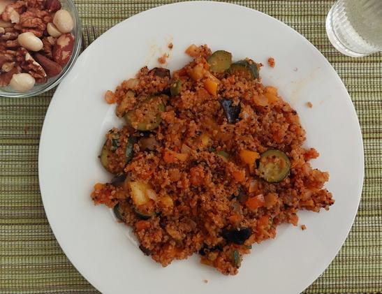 Das fertige Gericht, mit Quinoa ergänzt, auf einem weißen Teller. Links oben daneben ein Glasschälchen Nussmix und rechts oben ein Wasserglas. Alles auf einem grünen Platzdeckchen.