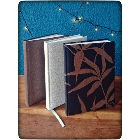 Drei A5 Bücher stehen nebeneinander auf einem Tisch. Von links nach rechts: Metallicbraun gepunktet/ weiße Krokodilschuppen/ Goldene Pflanzen auf Bronze.