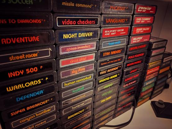 A wall of Atari 2600 cartridges in a shelf. Two game controllers laying in front of it