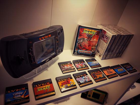 An Atari Lynx and some games and game boxes are sitting in a shelf.