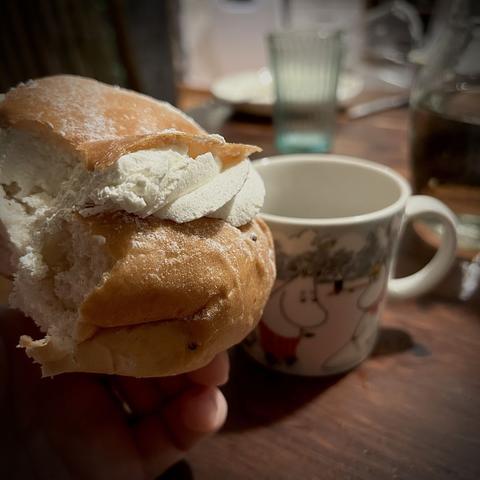A bun with cream in the middle, half eaten. A moomin coffee mug in the background.