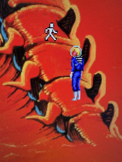 Pantallazo donde se ve en puro píxel art al protagonista Roger Wilco con un traje espacial azul con escafandra subiendo por un esqueleto gigante en un planeta de tierra rojiza. En la parte superior se ve el icono del ratón en forma de muñeco que anda. Toda la imagen tiene un filtro que trata de imitar el aspecto de un monitor CRT.