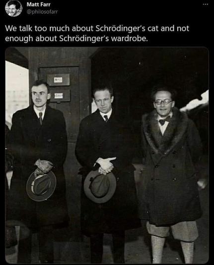 Three men standing on a train platform. The picture is black and white - from the thirties. Two of the men are dressed in suits and hold hats in their hands. Schrödinger is in a flamboyant fur-rimmed coat and knickers.