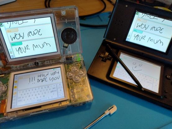 A black and a transparent DS Lite on a blue mat, engaged in a very immature pictochat session