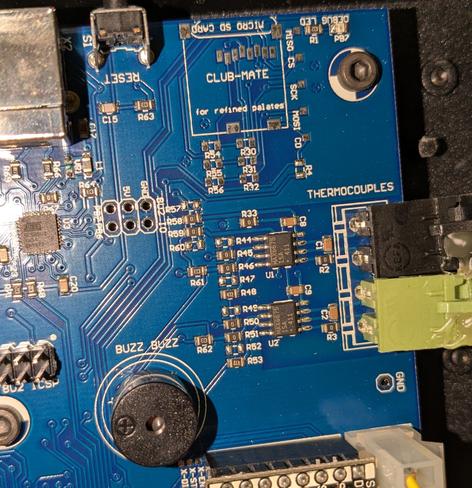 A wider view of one corner of a circuit board. Mostly normal components and expected markings, but the unused micro SD card mounting location at the top center has "CLUB MATE for refined palates" printed in it. At the bottom left, there is a small round speaker, but its label says "BUZZ BUZZ"