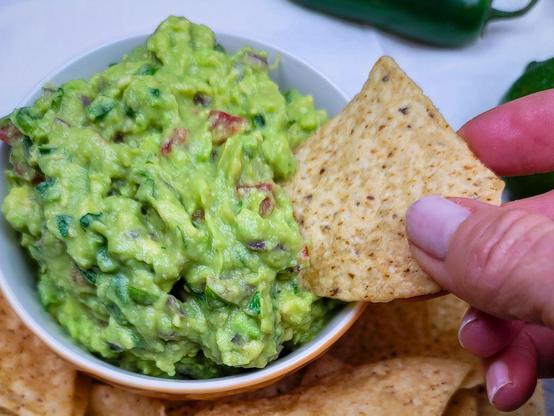A woman scoops up a chip full of homemade guacamole from a ceramic bowl.