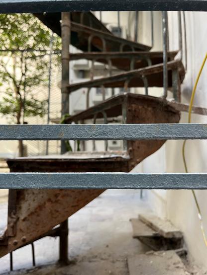 Behind the horizontal railings of a rear courtyard, a spiral staircase rises up the back of a small apartment building. Railings and staircase are both made of metal and probably date from the early part of the last century.