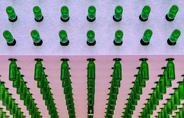 The image features multiple green bottles arranged in a geometric pattern. The bottles are arranged both pointing upwards and downwards in a mirrored fashion, creating a visually interesting and symmetrical effect. The perspective is such that it emphasizes the repetitive nature of the pattern.