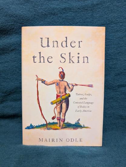 The book "Under the Skin" by Mairin Odle in front of a blue background