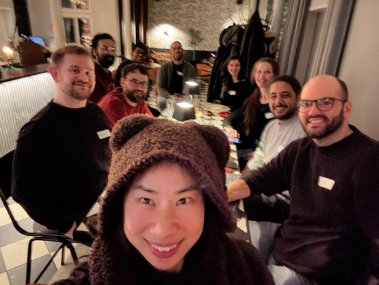 Image shows selfie taken by Dr Dingsu Feng (at the front) in brown furry hoody. It is taken in a cafe bar and there are a small group sitting at a table at a social event for researchers. This was the first postdoc social of 2025 and the traffic was stuck. Everyone had walked through heavy snow to get there.