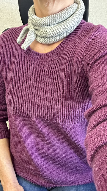 Wieder ein Klamotten-Selfie, wieder auf dem Bürostühl. Heute trage ich zur Jeans einen rot-lila Pullover aus Merino/Seide. Der obere Teil des Pullovers ist mit verschränkten Rippen gestrickt, der Rest glatt rechts.
Um den Hals trage ich wieder ein kleines kraus rechts gestricktes Halstuch in grünlich-grau.