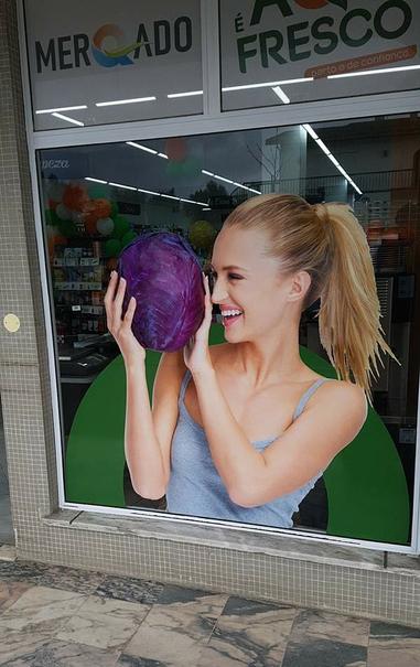 A photo of a small supermarket window. On the window is a gigantic picture attached of a blond, smiling girl that looks with delight at a red cabbage that she holds up in front of her face. 
Inside the shop you vaguely see the goods on shelfs.