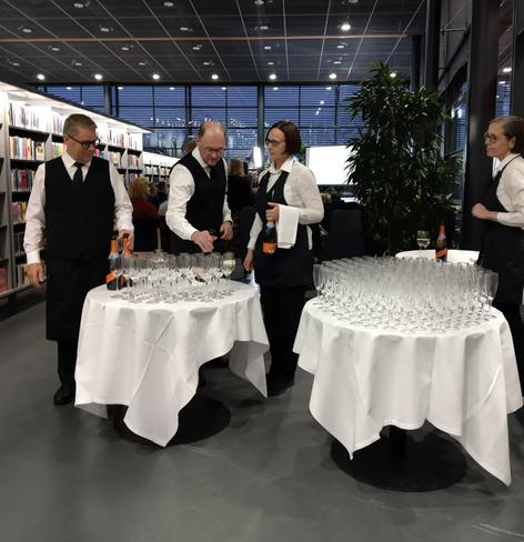 Neljä tarjoilijaa kaataa kuohuviiniä laseihin palkintojenjakoon saapuville