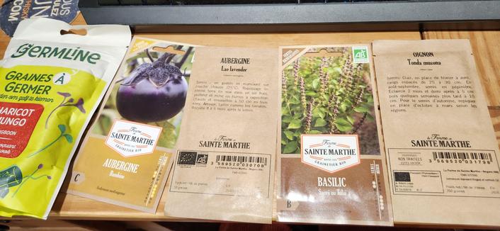 Sachets de graines, de gauche à a droite : 1 sachet de graines à germer haricots Mungo de marque Germaine. 4 sachets de graines de La Ferme de Sainte-Marthe : aubergine Bambino, Aubergine Lao Lavender, Basilic sacré ou Tulsi, oignon Tonda musona.