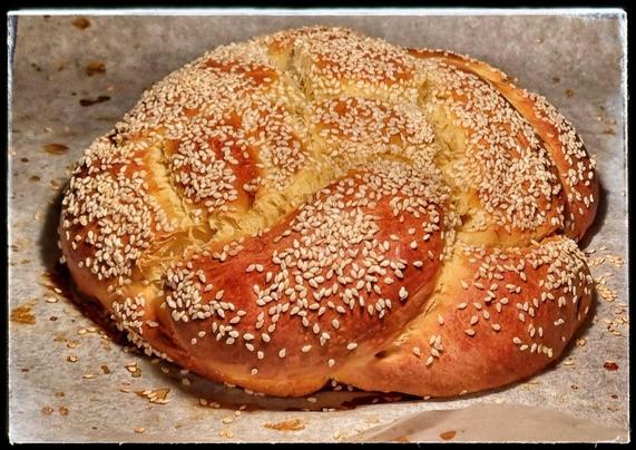 ein runder geflochtener Laib Challah (süßes Hefebrot), mit Sesamöl bestreut und goldbraun gebacken, auf Backpapier