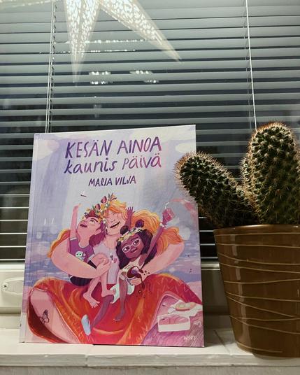 Ikkunalaudalla kirja, sen vieressä kaktus ruukussa. Ikkunasta heijastuu tähdenmuotoinen valaisin.