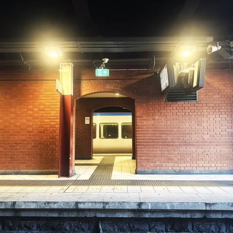 The view of a railway platform with a brick wall and a light on the left and right side of a tunnel, beyond which is a train carriage.