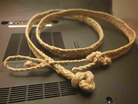 Ceinture en jute, partie plate tressée façon tissage, se transformant en tresse ronde, puis nœud de huit sur la tresse ronde.
De l'autre côté, la partie plate se plie pour faire un noeud d'écoute double d'ajut avec une cordelette deux brins torsadée qui a en son extrémité un noeud de chaise.
Le noeud de huit fait office de bouton qui se loge dans le noeud de chaise.
Très efficace et durable malgré une jute qui quoique douce au toucher est sensible à l'abrasion.