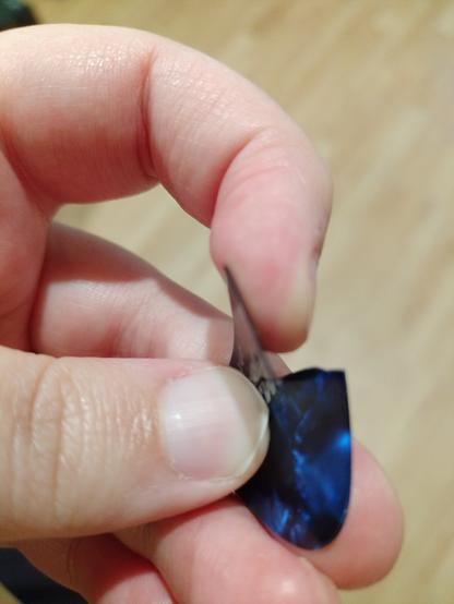 A hand holding a flimsy guitar pick, bending one side towards the camera to show off the giant crack in the middle of it.