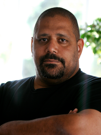 Photo of Brian J. Fox, a Black man with a buzz cut looking directly at the camera with a neutral facial expression. He is has black facial hair with a few white hairs. He is heavier set and wearing a black t-shirt with his arms folded.

He was born in 1959 and is a GNU hacker, programmer, entrepreneur, consultant, author, and free software advocate.