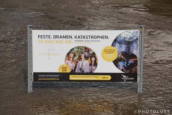 Im Hochwasser der Elbe in Dresden steht am Altstädter Ufer eine Werbetafel. Auf ihr steht „Feste. Dramen. Katastrophen.“