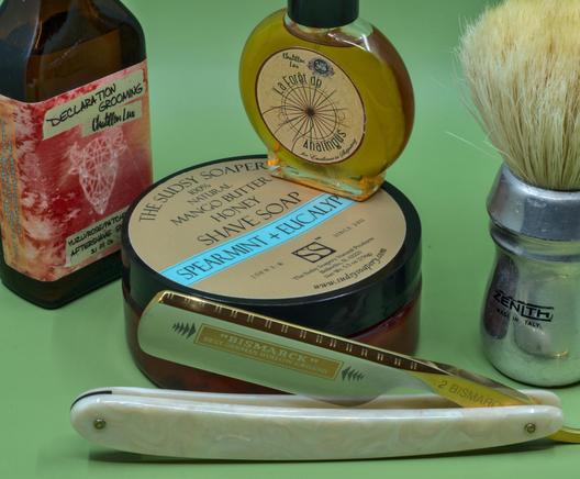 (ChatGPT description)

A refined wet shaving collection is arranged on a green background. At the center, The Sudsy Soapery’s Spearmint + Eucalyptus shave soap promises a refreshing lather. A Bismarck straight razor with a pearlescent handle rests elegantly in front. A Zenith shaving brush stands tall, while Declaration Grooming aftershave and Chatillon Lux La Forêt de L’Analogues fragrance add complexity to the ensemble. This setup embodies a luxurious and aromatic grooming ritual.