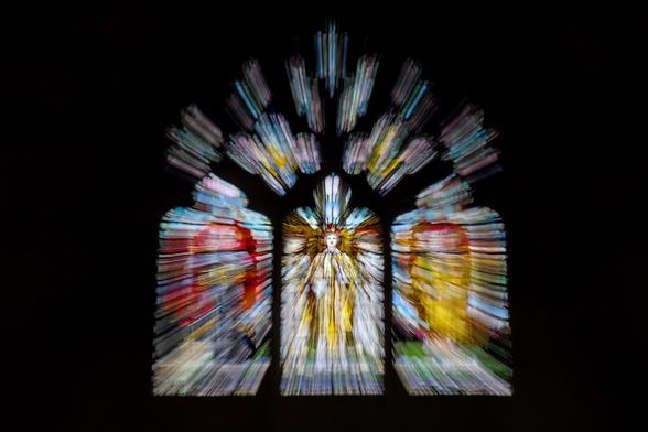 A stained glass window from a cathedral. The face of the angel in the very centre is clear, but all the rest of the window has beams of light shooting out, created by zooming the lens as the exposure is taken.
