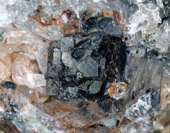 A dark boxy crystal with hints of red on the right hand side from where I broke it a bit. It's attached to a matrix comprised of clear quartz.
