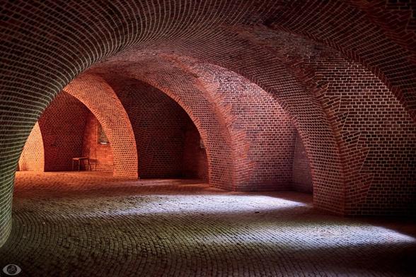 A circle with a solid brick wall to the left which arches to arching niches to the right (4 of them can be seen.) Every niche has a small window. Everything built out of red bricks, even the floor. The bricks on the floor are worn (but generally in good condition,) everything else is well preserved.