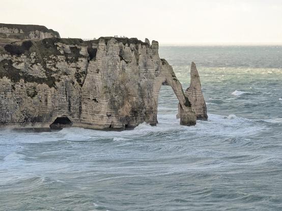 the impressive cliffs of etretat in Normandy, France. Their characteristic is to form a huge arch over the ocean. The picture is taken from a high point on a stormy but sunny day. The ocean is raging