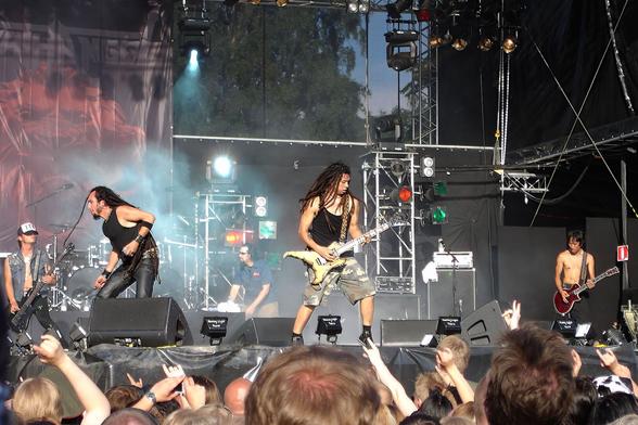 Death Angel esiintymässä Tuskan päälavalla 2004. Kuvassa keskellä toinen bändin kitaristi. Kuvassa myös kaikki muut bändin jäsenet paitsi rumpali. Kuvan alalaidassa paljon yleisöä takaa päin nähtynä.