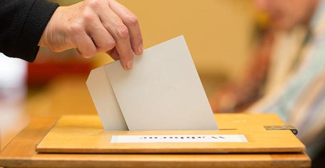 Das Bild ist ein Symbolbild für Wahlen und zeigt eine Person bei der Stimmabgabe. Als Nahaufnahme sieht man eine Hand, die den Wahlzettel in die Wahlurne steckt. Das Foto stammt von AdobeStock/Christian Schwier.