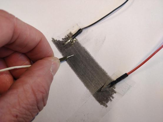 A photo of a piece of paper. On the paper, a patch of dark graphite has been drawn with a pencil, about 5 cm long and 2 cm wide.

Two wires, one black and one red, have their ends taped to the outer edges of the graphite patch.

On the left a hand is seen holding a third, white, wire with it's end pushing against the graphite, close to the edge where the black wire is attached.

Graphite is quite conductive, but also have a relatively high resistivity. This means that the patch of graphite conducts current, but can have a resistance in the range of a few kOhms to MOhms depending on how wide, thick and long you make the patch.

By moving the white wire back and forth on the graphite patch between the two other wires, the resistance between the middle wire and the other wires varies. Closer means less resistance and vice versa.

This exactly mimics how a potentiometer works. By using only one of the edge wires you can instead mimic a rheostat. Only using the edge wires makes a regular resistor.