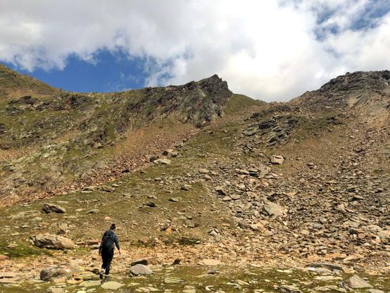 A woman is walking on coarse gravel. She's about to go zigzag up the mountain's side.