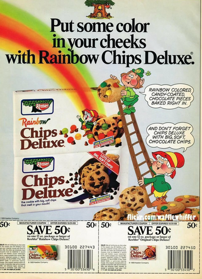 Two packages of chocolate chip cookies. The top one has rainbow M&M like candies. The Keebler elves are climbing up a ladder as a rainbow touches down upon them.