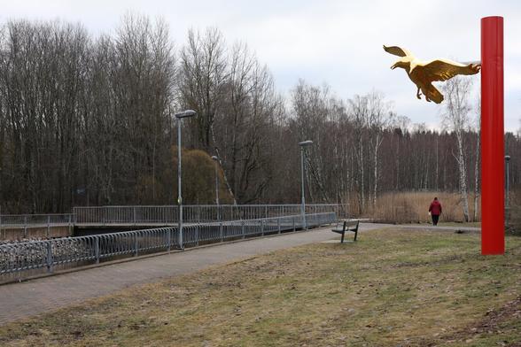 A photo of a person feeding mallards. There is a red pole and a golden statue of a two-headed eagle on the right.