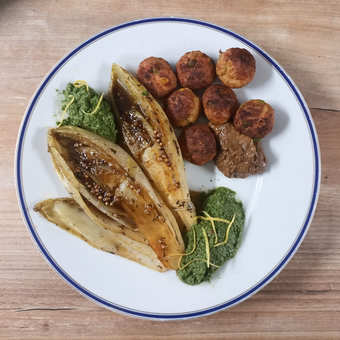 2 halbe Chicorée auf dem Teller, 7 Hackbällchen mit Senf, grünes Pesto mit Zitronenzesten, auf dem Chicorée etwas Sauce mit Korianderkörnern.