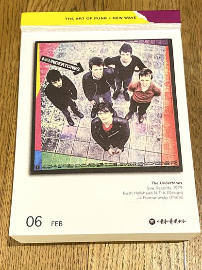 Das Bild zeigt ein Cover oder Poster der nordirischen Punk-Rock-Band The Undertones. Die fünf Bandmitglieder stehen auf einem gefliesten Boden und blicken aus einer Vogelperspektive nach oben in die Kamera.

Das Foto hat eine farblich bearbeitete, leicht körnige Ästhetik mit einem bunten Rand in Rot, Gelb, Blau und Grün. In der oberen linken Ecke befindet sich ein schwarzer Pfeil mit weißer Schrift, auf dem “The Undertones” steht. Unten am Rand sind Liedtitel aufgelistet, was darauf hindeutet, dass es sich um ein Album- oder Single-Cover handelt. Die Bandmitglieder tragen lässige Kleidung, darunter Lederjacken und Pullover, passend zum Stil der späten 1970er oder frühen 1980er Jahre.