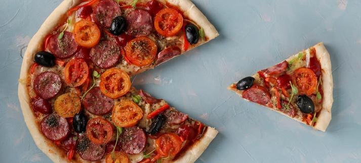 Pizza with a cut out piece on a light blue background, top view / Angelika Mostova