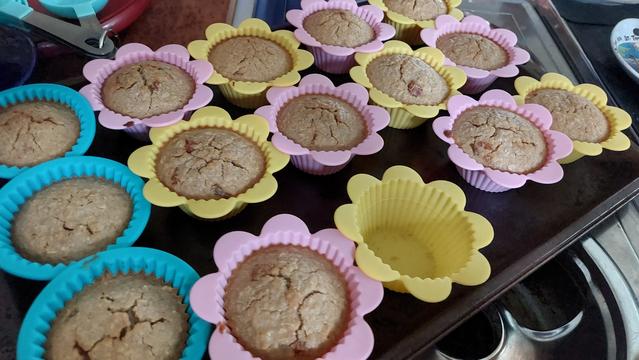 A bunch of oatmeal muffins in individual silicone muffin cups, some shaped like flowers, on a tray. One cup is empty.