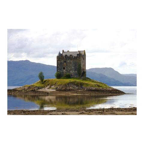 Sur un îlot tapissé d'herbe, un ancien château en pierres de forme carrée, d'époque médiévale. Dans un arrière plan lointain se découpent des montagnes sous un ciel couvert.