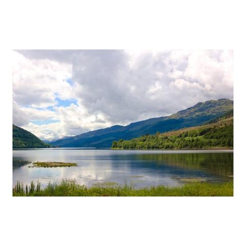 Sous un ciel nuageux, une grande étendue d'eau encadrée de montagnes verdoyantes.