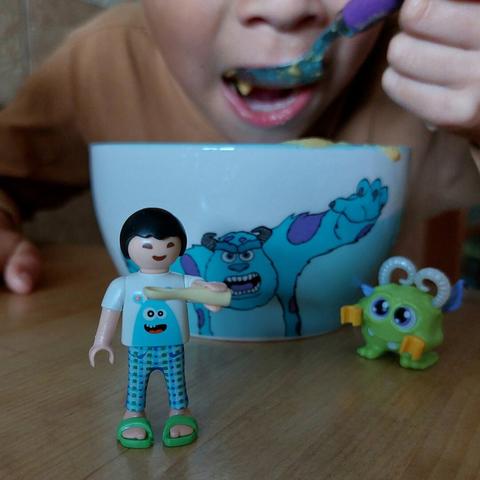 Criança a comer a sopa num prato com a imagem de um monstro azul. E à frente um playmobil criança com uma colher na mão