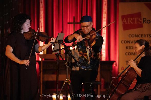 The three musicians of Trio Fadolín playing violin, fadolín and cello, in concert at a church (in Nyack, NY) .  Their faces are dimly lit.