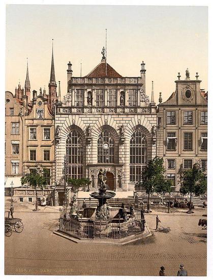 This image depicts a historic building, likely the Exchange and Artushof in Danzig (now Gdańsk), West Prussia. The scene is set within what appears to be Market Square, showcasing an elaborate structure with Gothic architectural elements such as pointed arches and intricate stonework. A central fountain serves as a focal point before the grand facade of the building, which features statues adorning its corners, large arched windows, and ornate detailing around the entranceway.

Surrounding buildings exhibit similar historical charm but in more modest styles with gabled roofs and dormer windows. People can be seen strolling about or engaging in daily activities on what seems to be a paved plaza, adding life to this historic setting. The overall ambiance of the image conveys an atmosphere reflective of late 19th-century Europe, complete with horse-drawn carriages hinting at transportation methods from that era.

The photograph's sepia tone and soft focus suggest it was taken during or shortly after its creation in the timeframe between ca. 1890 to ca.
