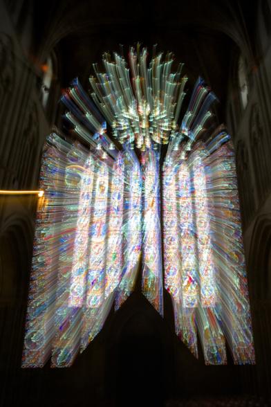 A large stained glass window with light streaming through. By zooming while taking the shot it seems that the light is projecting another copy of each pane in the window, into the air in front of it. The walls of the cathedral are just about visible around the window.
