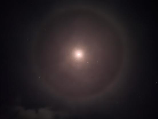 La luna, como un punto brillante en el centro de la imagen. rodeada por una aureola perfecta de color rosado.